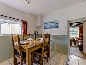 A dining area with a wooden table set for four, a vase with flowers, and a painting on the wall. - 2 Bed in Bideford (oc-fordm) (Woolfardisworthy)