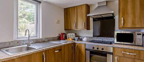 A modern kitchen with wooden cabinets, a stainless steel sink, a microwave, and a gas stove.