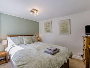 A bedroom with a bed, a nightstand, a TV stand, and two wall-mounted flower paintings. - 2 Bed in Bideford (oc-fordm) (Woolfardisworthy)