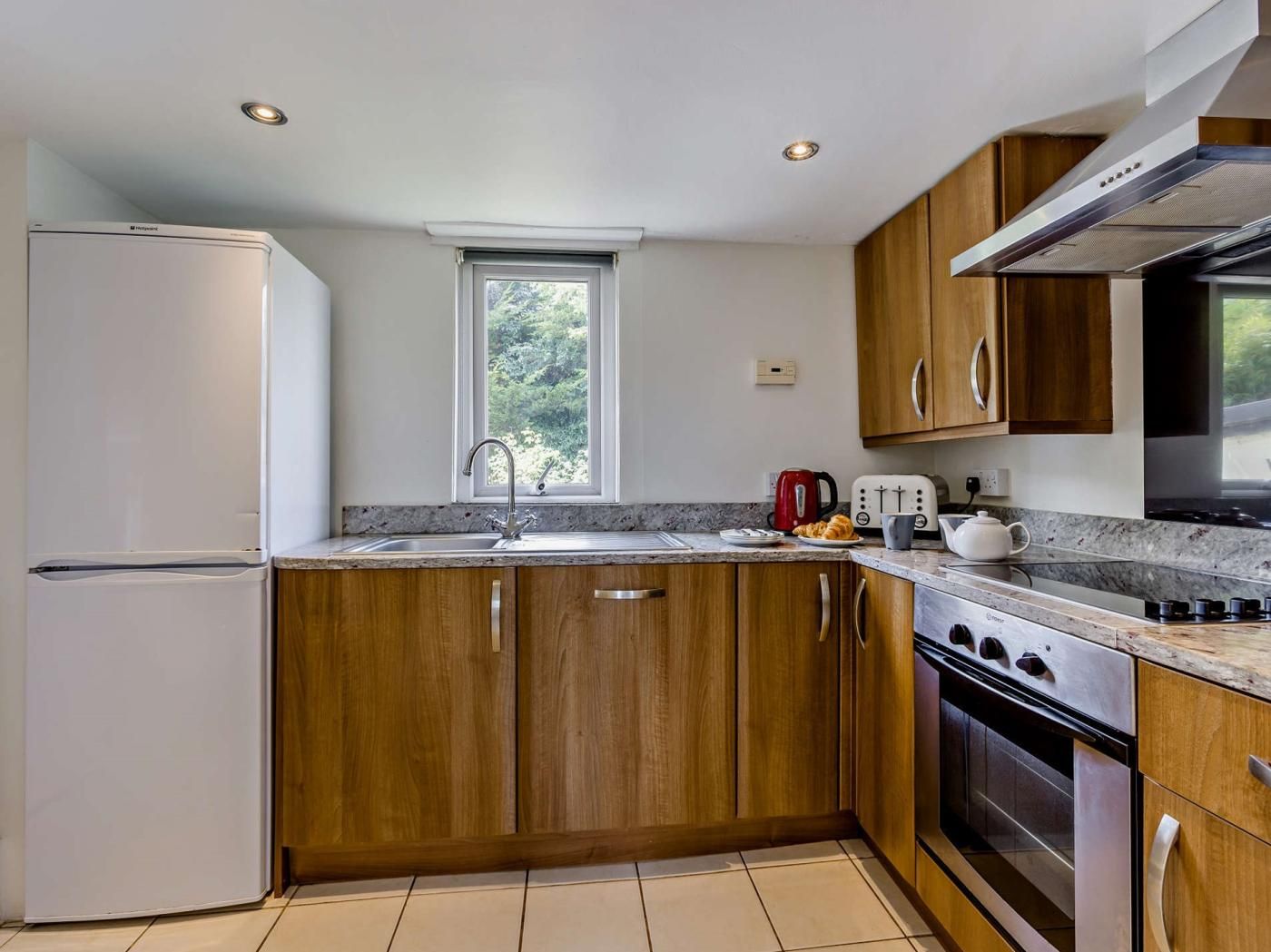 A modern kitchen with wooden cabinets, a stainless steel refrigerator, a window, and a built-in oven.