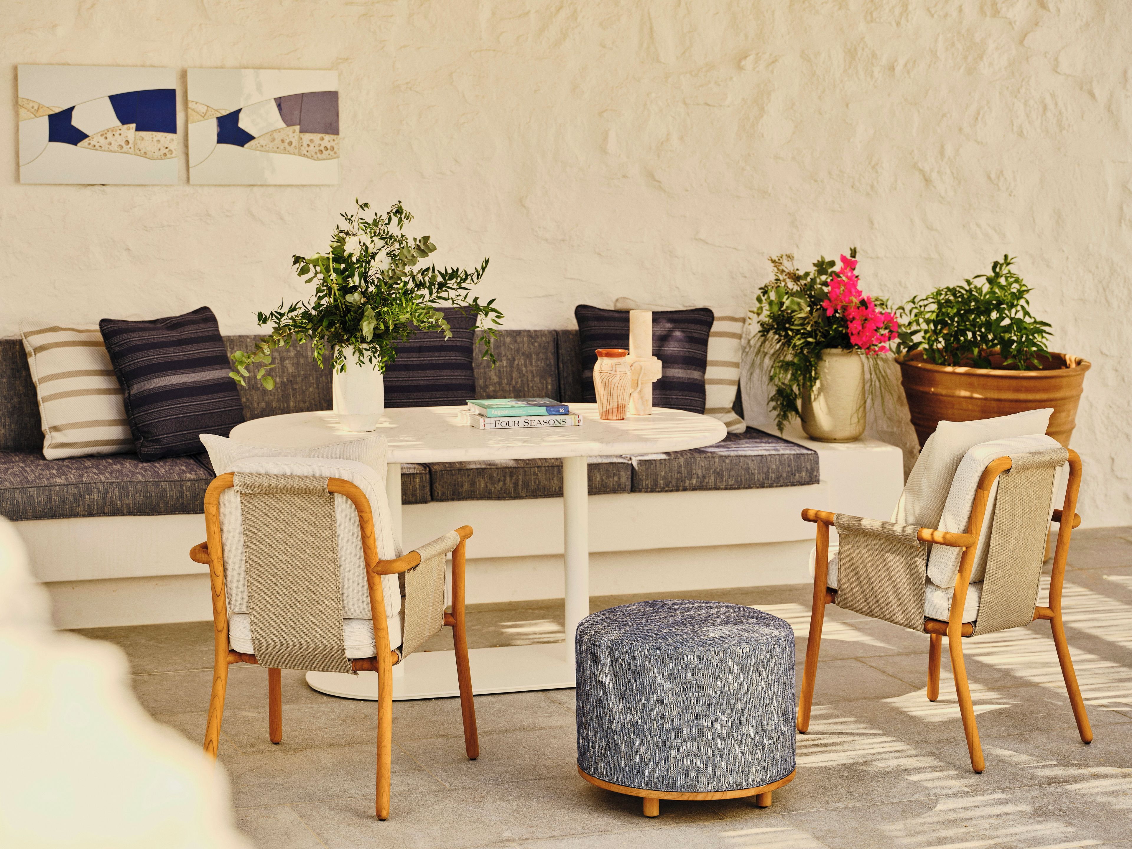 Una sala de estar moderna con una mesa redonda blanca, dos sillas de madera, un sofá con cojines a rayas y varias plantas en macetas.