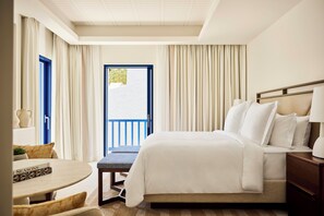 A hotel room with a bed, bedside table, lamp, and a view of the outdoors.