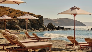 A beach with lounge chairs and umbrellas, rocky cliffs in the background, and a clear view of the ocean.