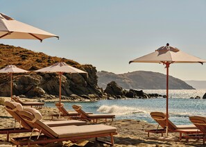 A beach with lounge chairs and umbrellas, rocky cliffs in the background, and a clear view of the ocean.