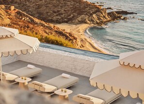 Un área de descanso en la playa con tumbonas y sombrillas, con vistas a una costa rocosa y una playa.