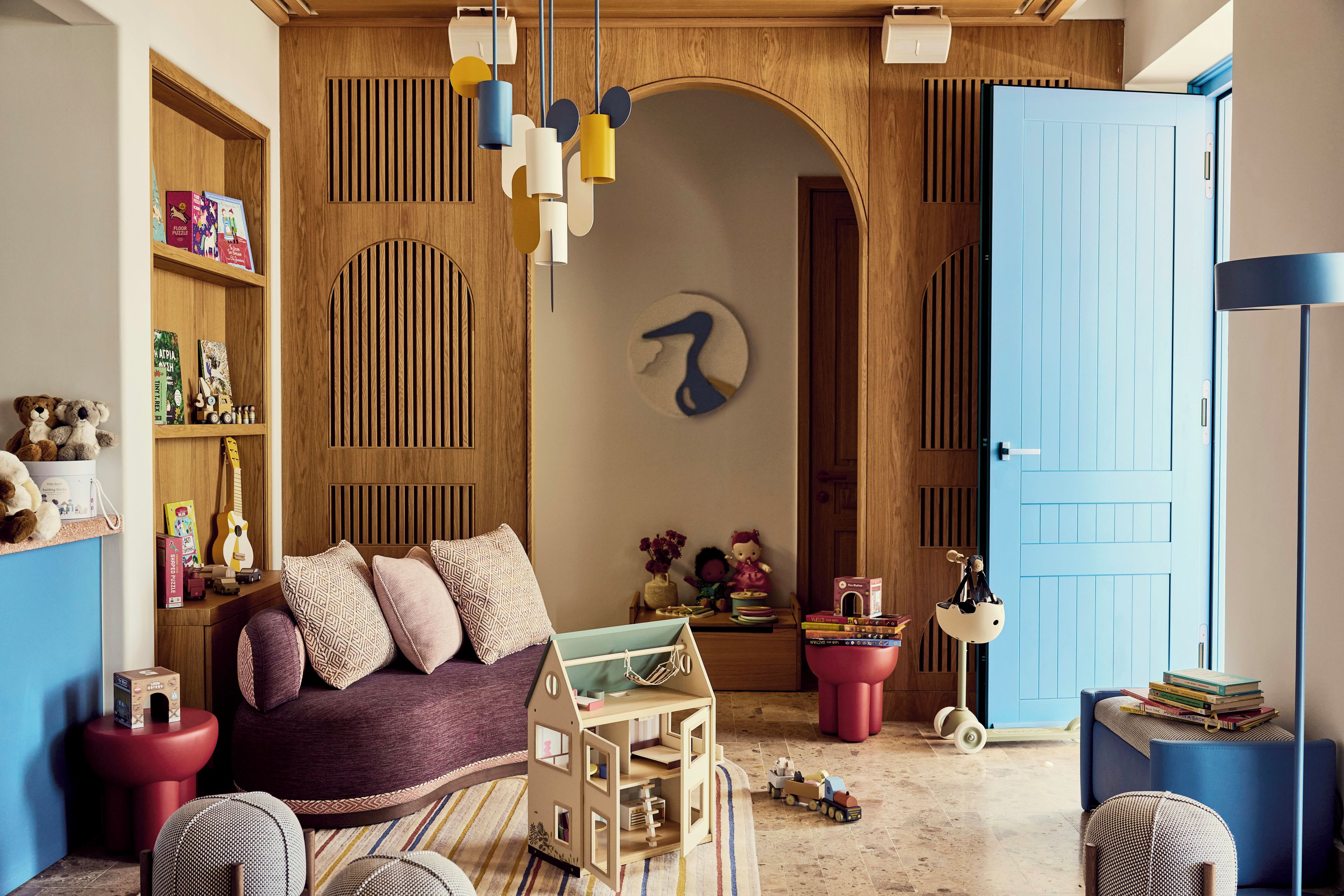 Um quarto acolhedor com porta de madeira, sofá vermelho, uma casa de madeira pequena e diversos brinquedos e livros.