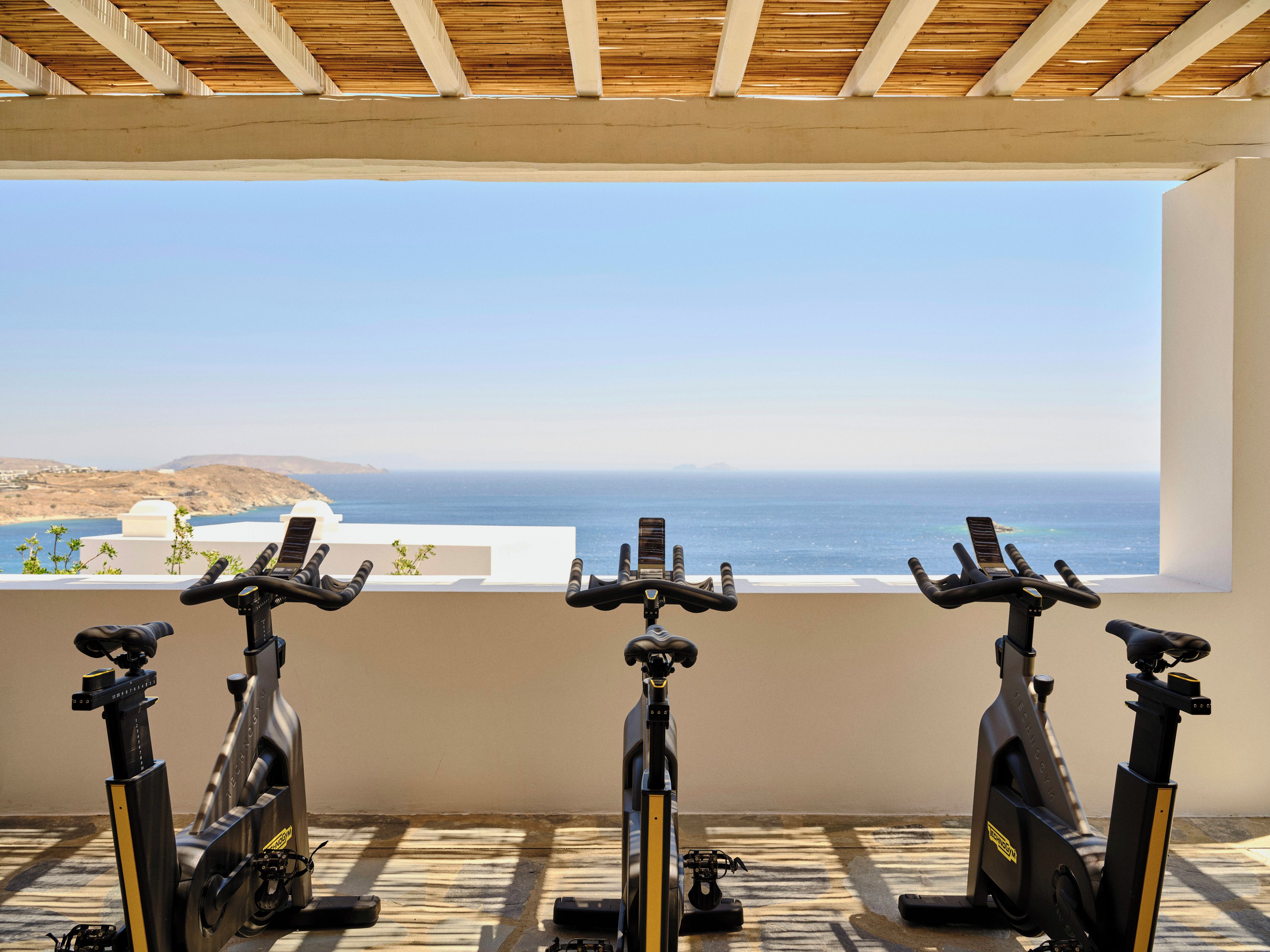 Três bicicletas ergométricas lado a lado, com vista para o oceano.