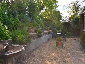 Un jardin avec un barbecue, des plantes en pot, un mur de briques et un banc.