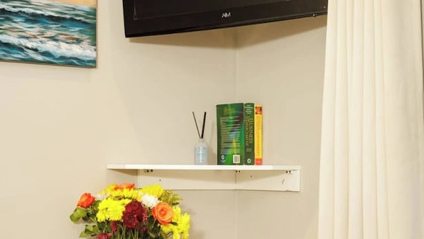 Ein Zimmer mit einem Bett, einem Schreibtisch mit Blumen, einem Flachbildfernseher und einem Bild an der Wand.
