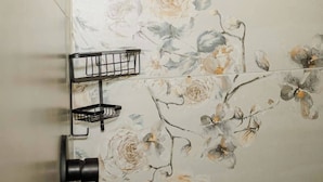 Eine Dusche mit blumigem Wandpapier, einem schwarzen Duschkopf und einem schwarzen Handtuchhalter.