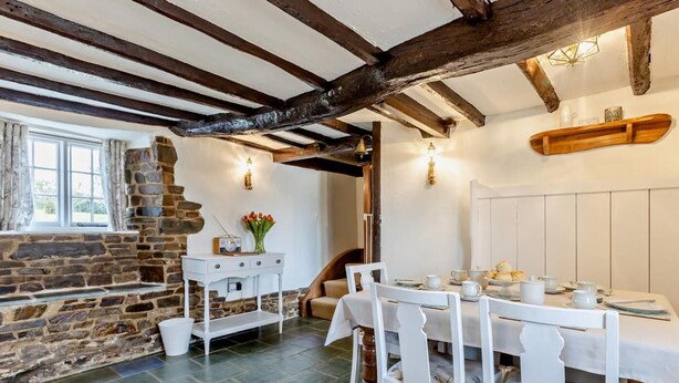 A dining area with a stone wall, wooden beams, a white table set for four, and a radio on a small table. - 3 Bed in Bude (oc-heyle) (Launcells)