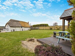 A thatched-roof house with a grassy yard and a wooden deck with a picnic table. - 3 Bed in Bude (oc-heyle) (Launcells)