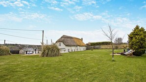 A thatched-roof house with a well-maintained lawn and a small tree. - 3 Bed in Bude (oc-heyle) (Launcells)