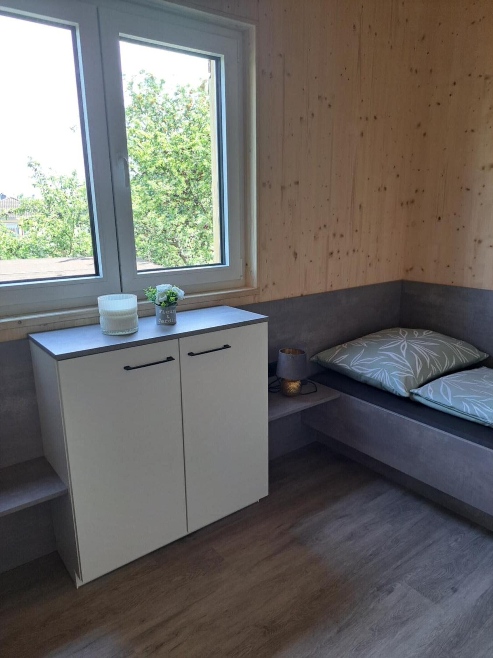 A bedroom with a window, a bed, a bedside table, and a wardrobe.