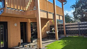 A two-story wooden house with a balcony, a patio with outdoor furniture, and a well-maintained lawn. - Apartment 'Ferienappartement Coleen' with Private Terrace, Balcony and Wi-Fi (Höchst)