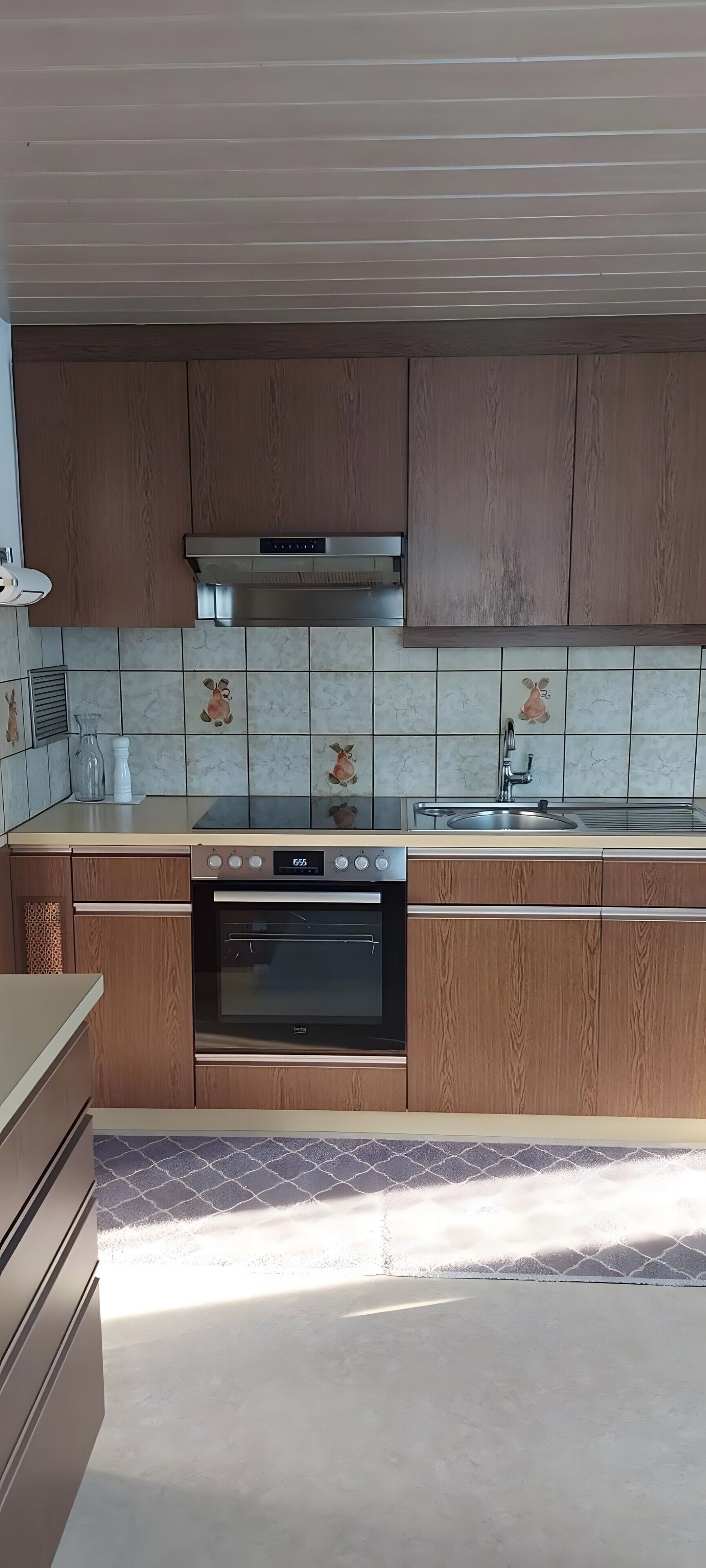 Een moderne keuken met houten kastjes, een roestvrijstalen afzuigkap, een ingebouwde oven en een betegelde spatwand met dierenmotieven.