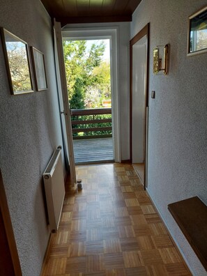 Un pasillo con un radiador, un banco y vista a un balcón con vegetación.