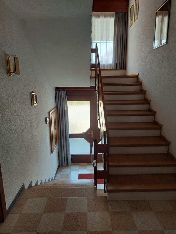 Escada de madeira com corrimão, levando a uma porta com vista para o exterior.