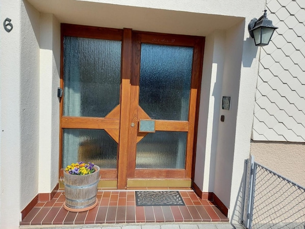 A double wooden door with glass panels, a metal bucket with flowers, and a metal gate.