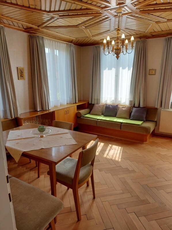 Una habitación acogedora con techo de madera, una mesa de comedor con sillas, un sofá con cojines y una araña.