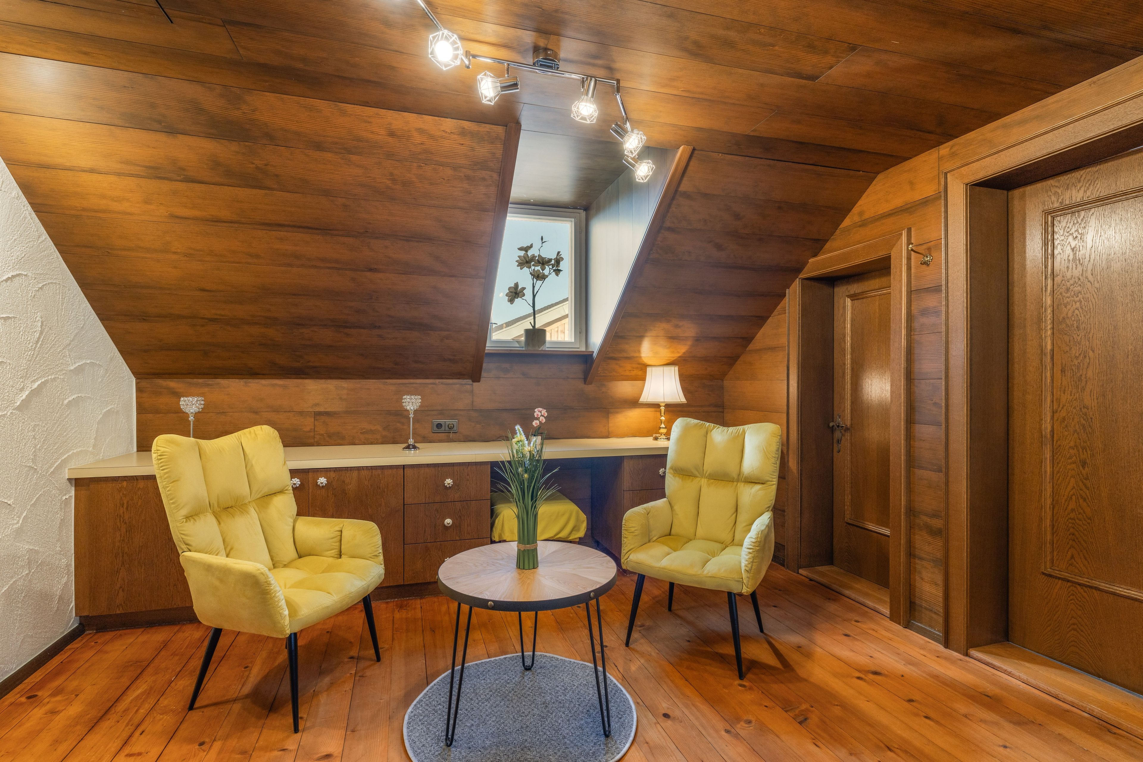 Ein Zimmer mit Holzboden und -wänden, einem runden Tisch mit zwei Stühlen, einer Lampe und einem Fenster mit Blick.