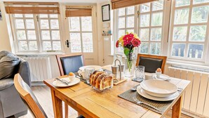 Comedor con una mesa de madera, sillas, un jarrón de flores y vistas amplias a través de grandes ventanas.