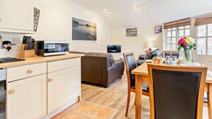 Una cocina moderna con microondas, zona de comedor con mesa y sillas, sofá y televisor.