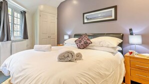 Una cama bien hecha con una toalla enrollada, una almohada y un control remoto sobre una mesita de noche.