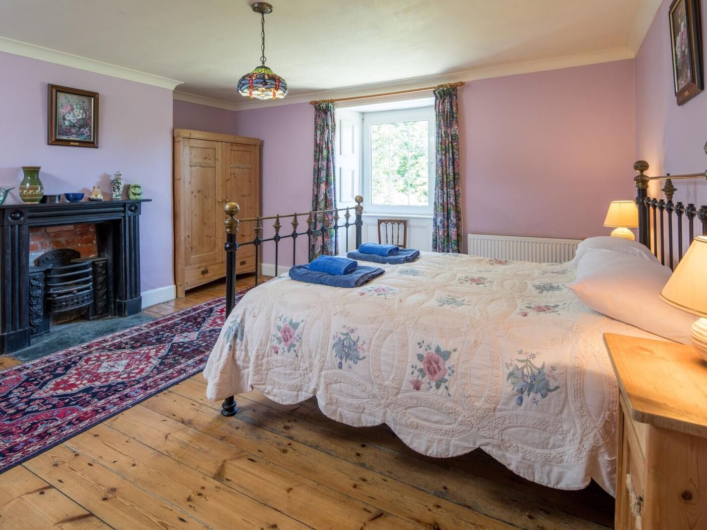 A bedroom with a bed, a fireplace, a window with curtains, and a wooden floor.