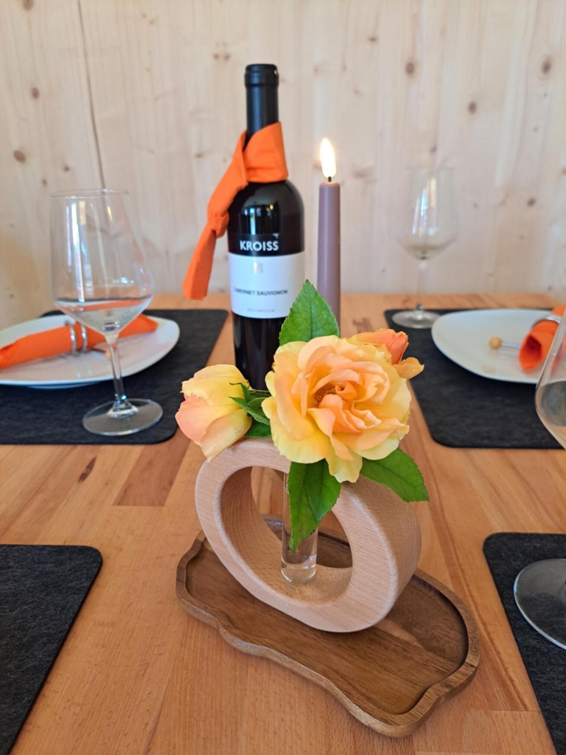 A table setting with a bottle of KROISS wine, a candle, and a vase with flowers.