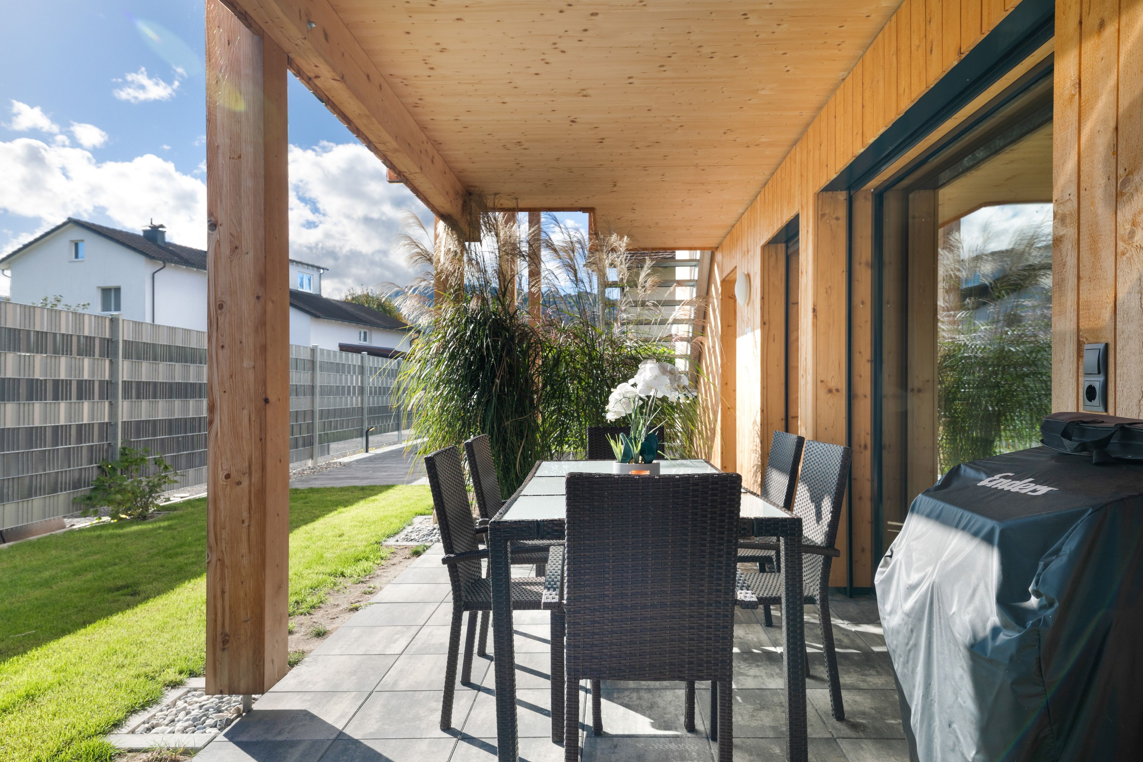 Een terras buiten met een tafel en stoelen, een overdekt gedeelte en uitzicht op de omgeving.
