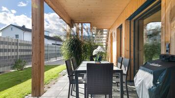 Een terras buiten met een tafel en stoelen, een overdekt gedeelte en uitzicht op de omgeving.