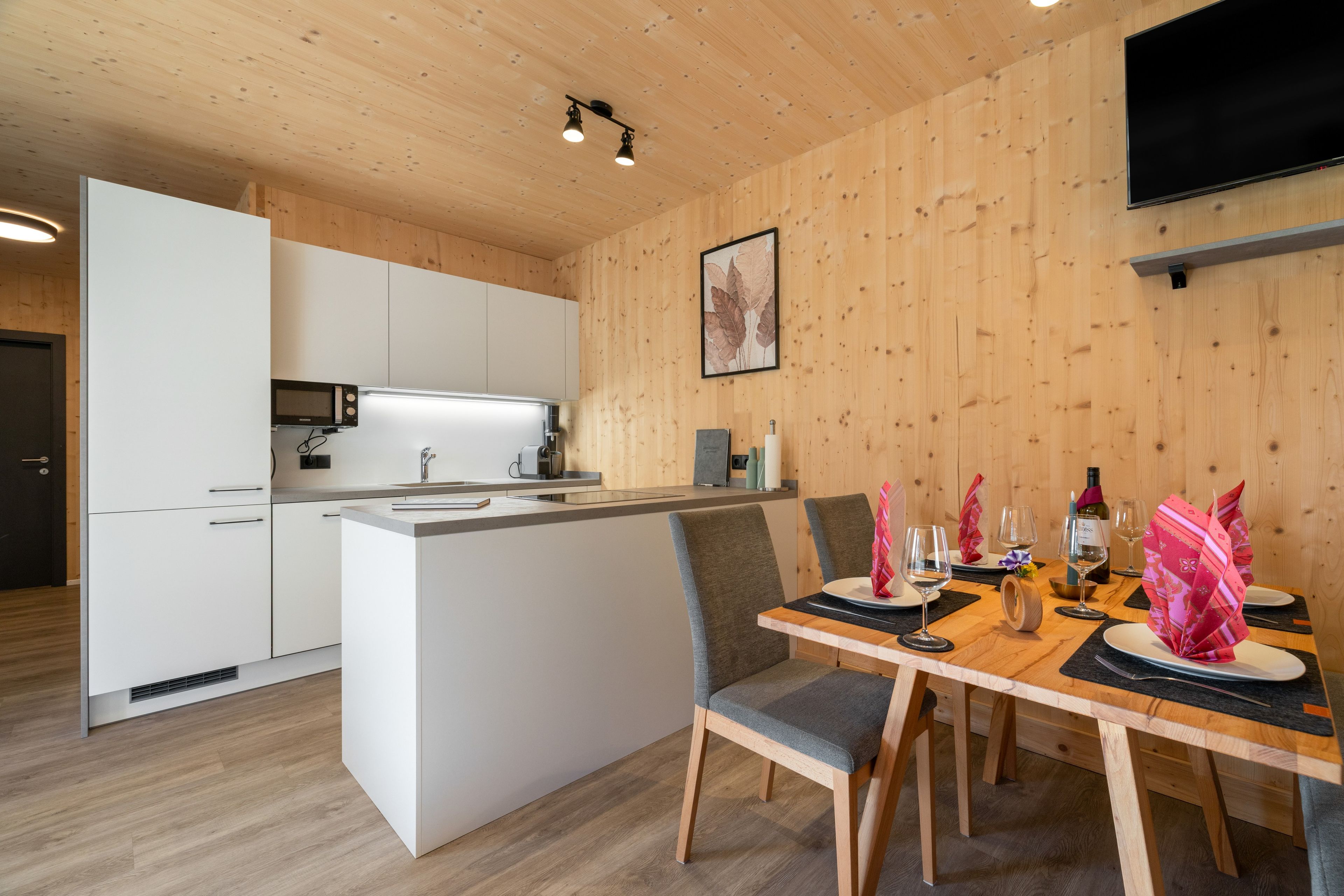 Et moderne køkken med en central ø, hvide skabe og et spiseområde med et bord dækket til to personer.