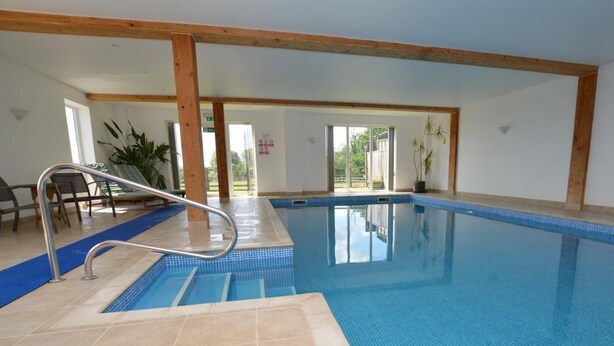 Una piscina interior con agua azul cristalina, una escalera metálica y vistas al exterior a través de amplios ventanales.