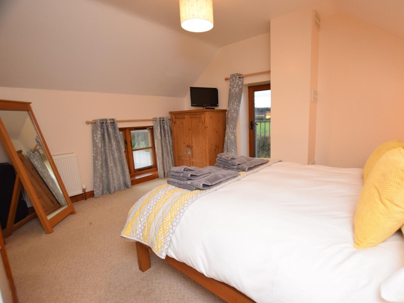 A bedroom with a bed, a wooden wardrobe, a mirror, and a television.