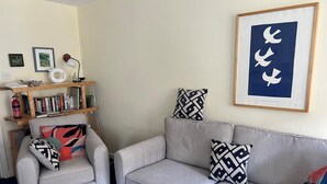A living room with a grey sofa, armchair, and coffee table. There is a bookshelf with books and decorative items. A framed picture with white birds hangs on the wall. - 1 Bed in Edinburgh (oc-e1887) (Edinburgh)