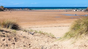 En bred, sandet strand med et fyrtårn i det fjerne, klare himmel og roligt hav.