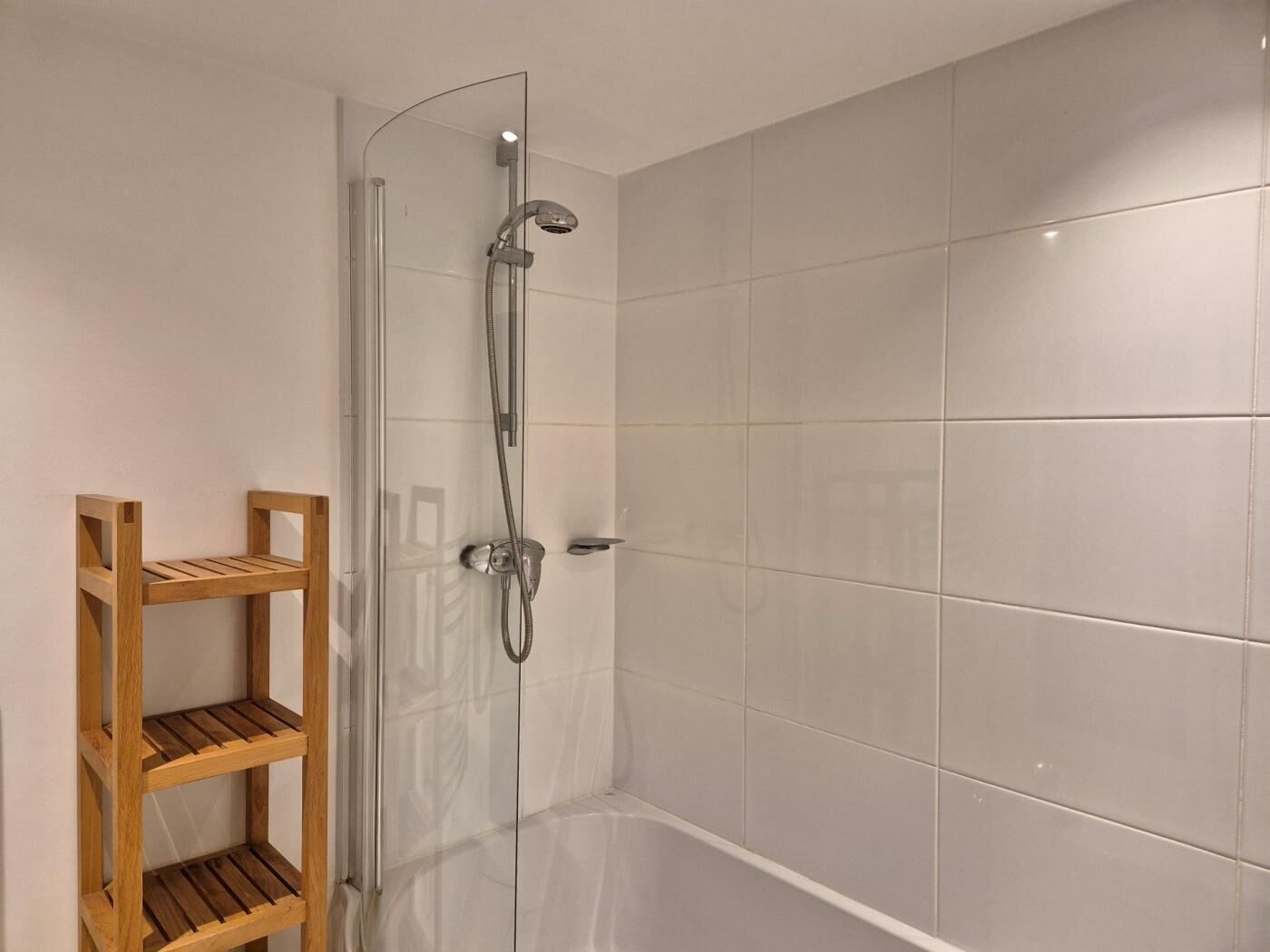 Cabina de ducha con puerta de vidrio, cabezal de ducha de mano y panel de control en la pared.