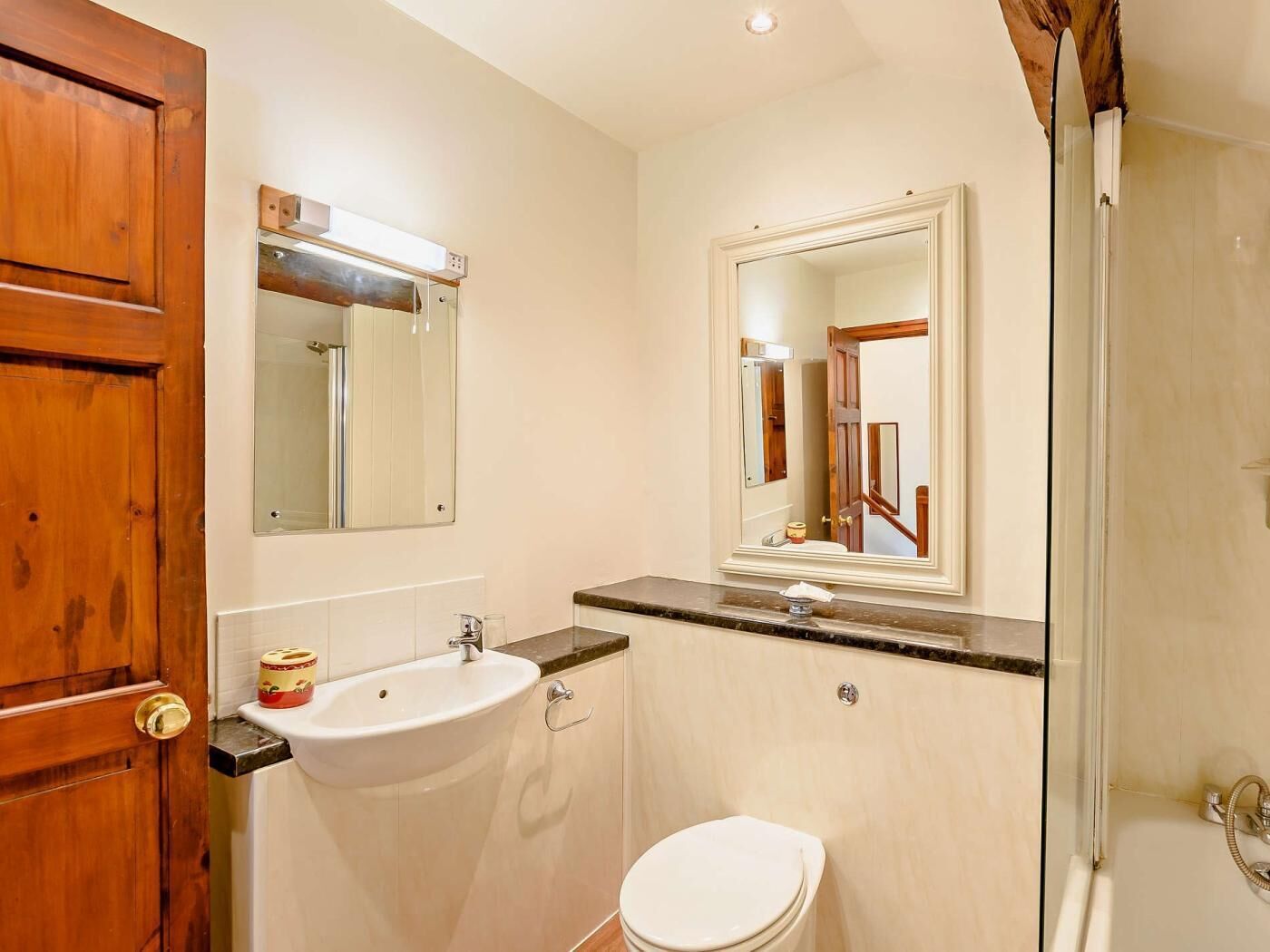 A bathroom with a wooden door, a sink, a toilet, and a shower.