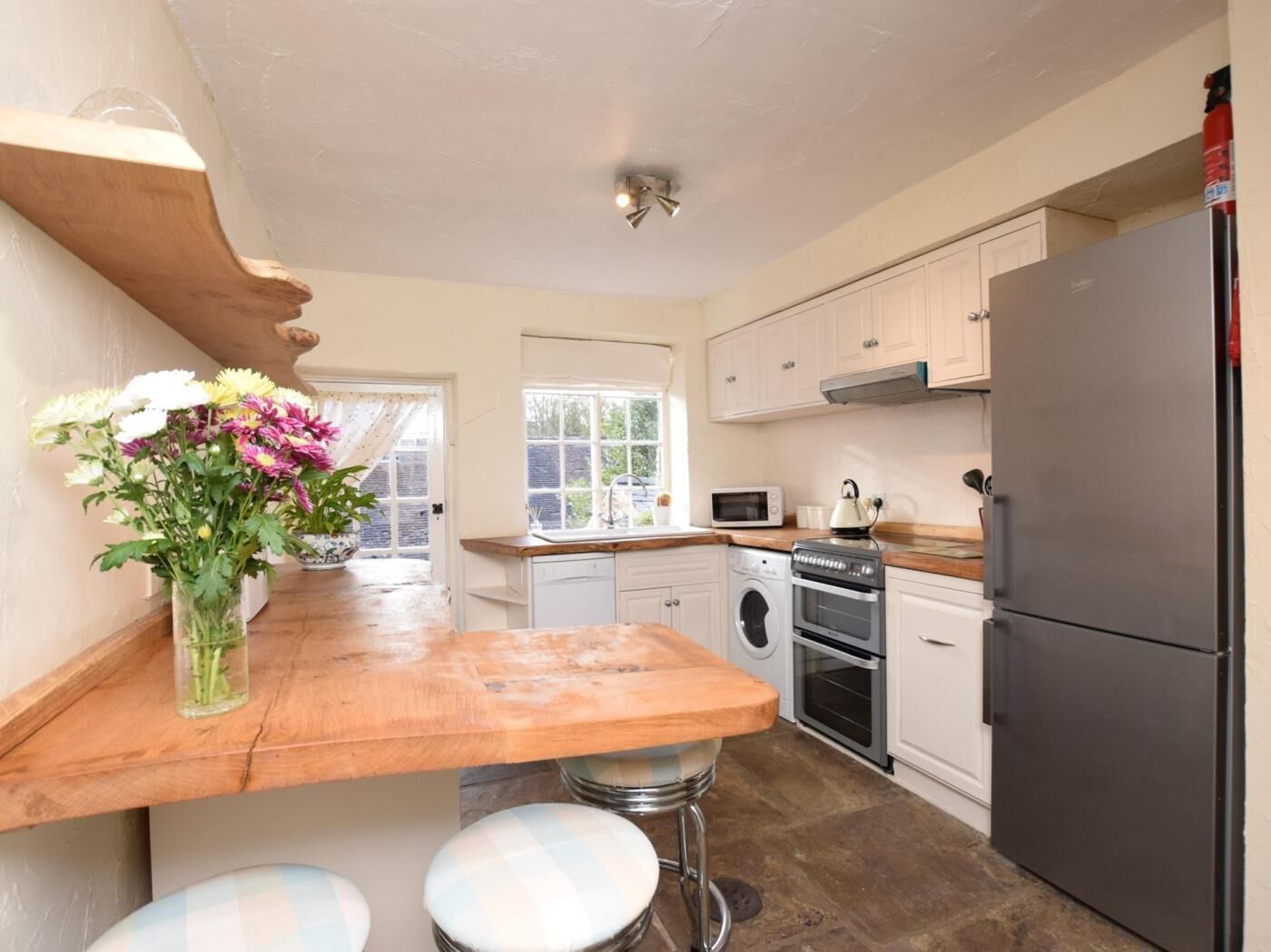 A kitchen with a wooden countertop, a washing machine, an oven, a microwave, and a refrigerator.