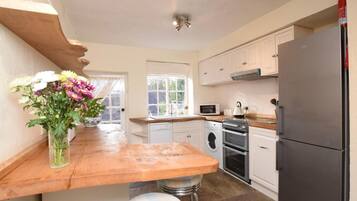A kitchen with a wooden countertop, a washing machine, an oven, a microwave, and a refrigerator.