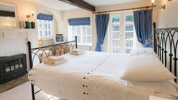A bedroom with a bed, a dresser, a mirror, a window with curtains, and a fireplace.