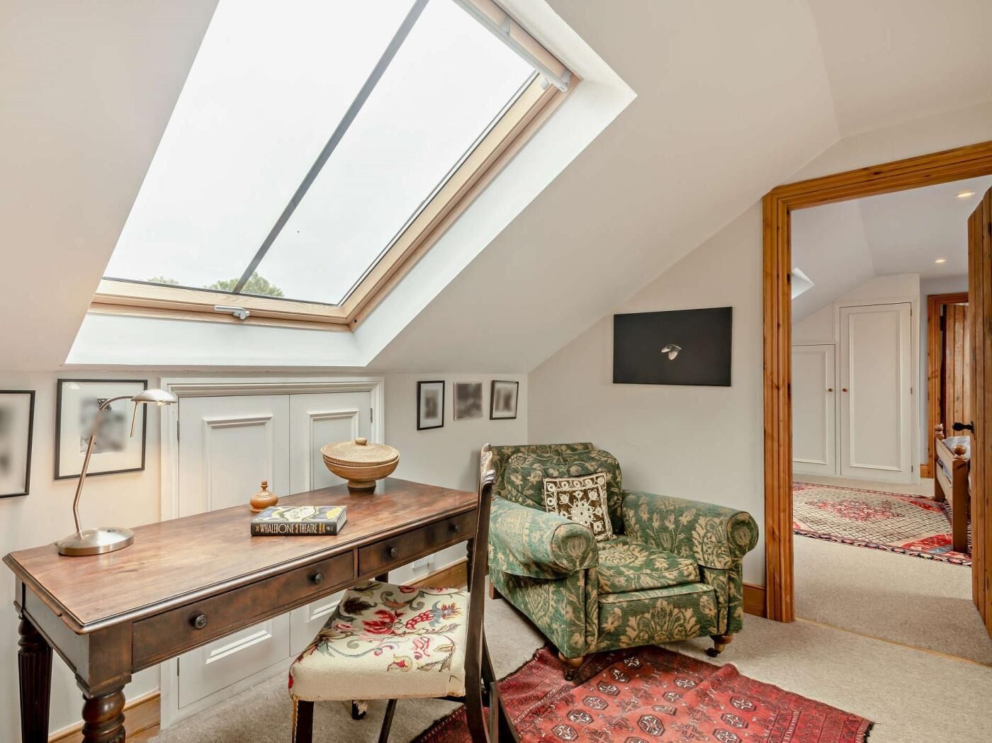 A room with a skylight, a desk, a green armchair, and a patterned rug.