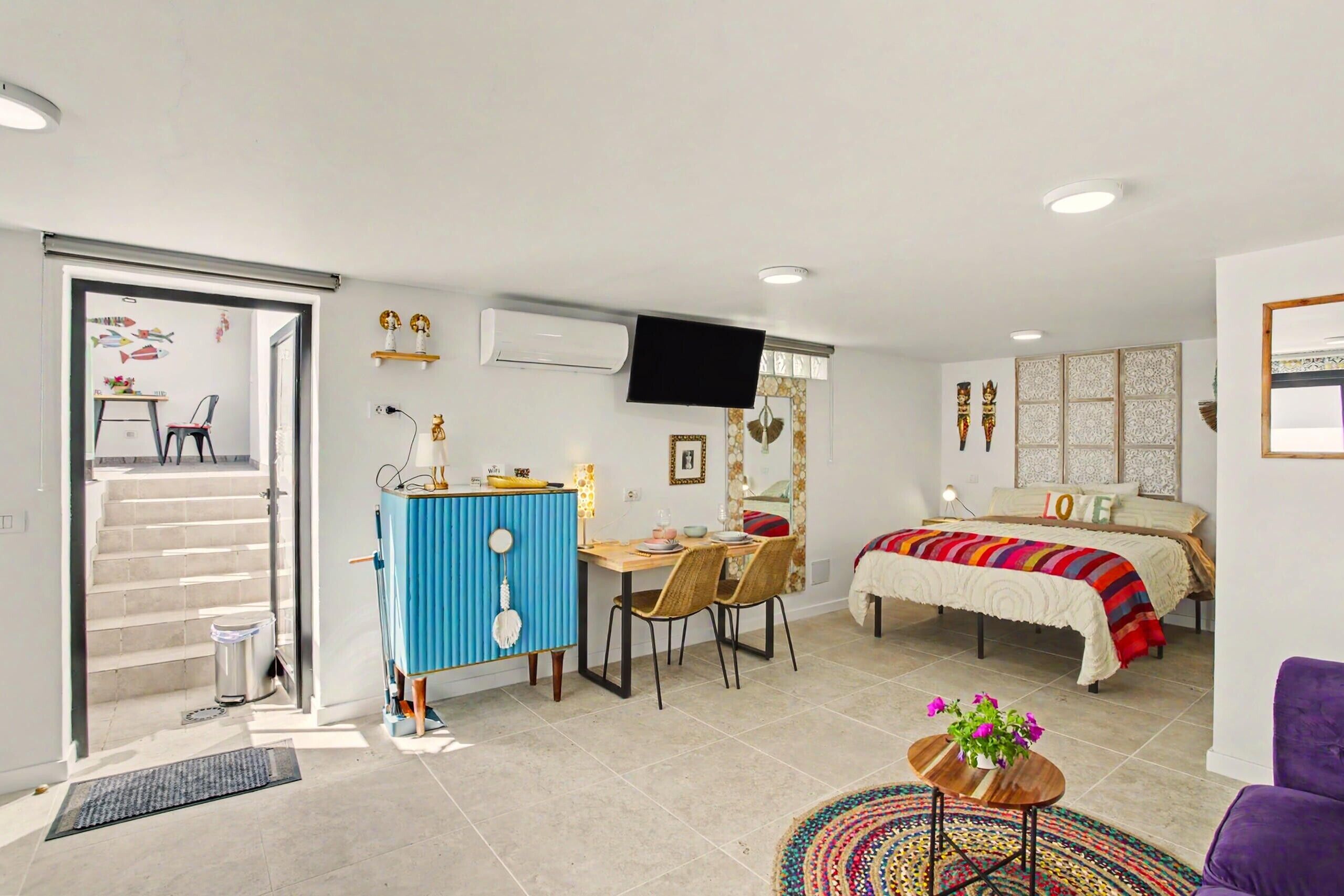 A compact living space with a bed, a desk, a chair, a television, and a staircase leading to an upper level.