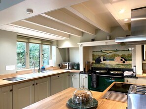 A modern kitchen with a large window, a microwave, a stove, and a tiled backsplash. - 4 Bed in Whitby (oc-g0042) (Goathland)