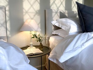 A neatly made bed with white linens, a bedside lamp, and a small table with a book and a vase of flowers. - 4 Bed in Whitby (oc-g0042) (Goathland)