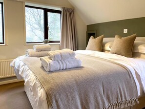 Ein ordentlich gemachtes Bett mit gefalteten Handtüchern, einer Decke mit Fischgrätmuster und Blick auf Bäume durch ein Fenster.