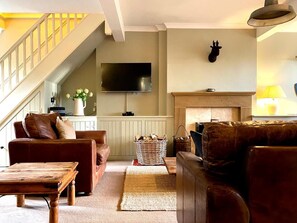 Ein Wohnzimmer mit Sofa, Couchtisch, Kamin, Fernseher und einer Treppe.