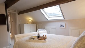 Une chambre avec un puits de lumière, un lit sur lequel est posé un plateau de petit-déjeuner, et des meubles blancs.
