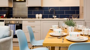 Een moderne keuken met een eettafel voor vier personen, lichtblauwe stoelen, een roestvrijstalen afzuigkap en een klok aan de muur.